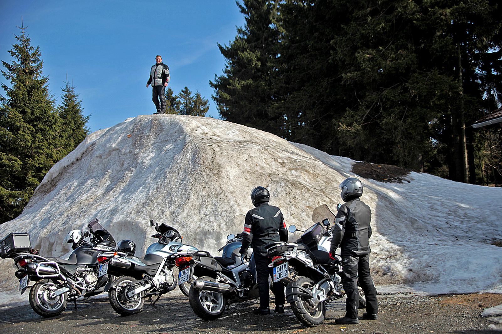 Hoher Haufen zusammengeschobener Altschnee, oben steht ein Mann, davor vier abgestellte Motorräder Hoher Haufen zusammengeschobener Altschnee, oben steht ein Mann, davor vier abgestellte Motorräder